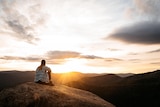 Woman sitting on a rock in the mountains looking at the sunset