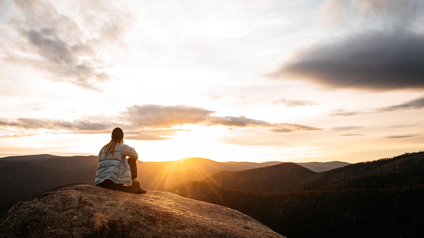 Woman sitting on a rock in the mountains looking at the sunset