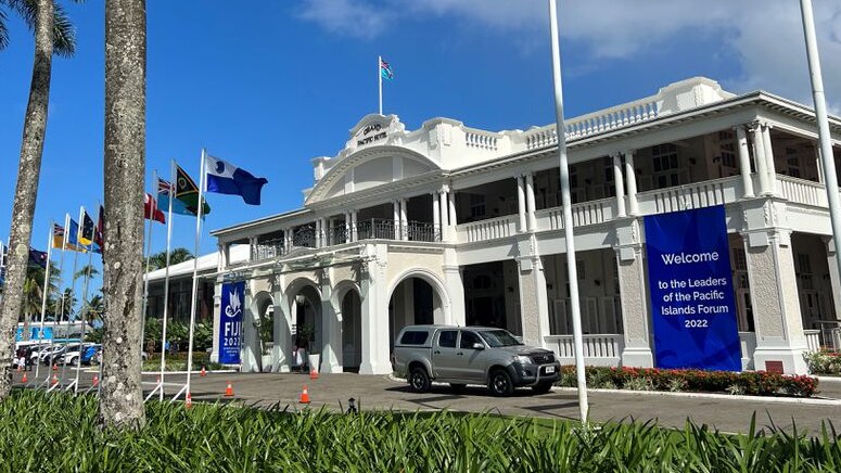 A general view of Grand Pacific Hotel, a white colonial building with pacific island flags flying on a blue-sky day