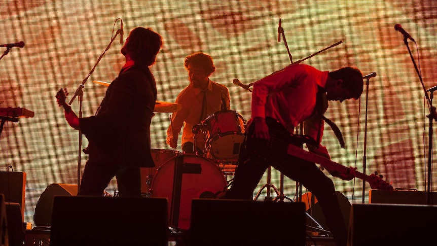 A band plays against a light up backdrop.