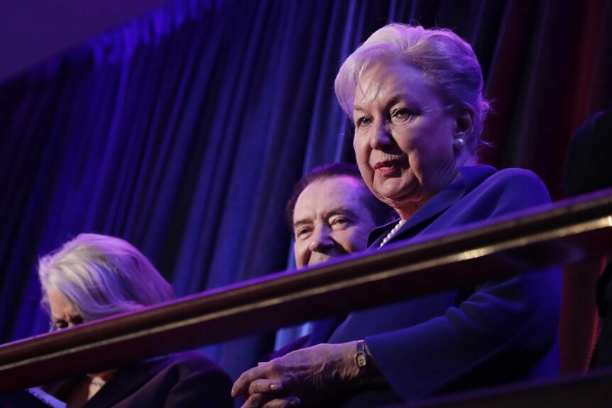 Maryanne Trump Barry wears blue and looks down from balcony. Two people are next to her.