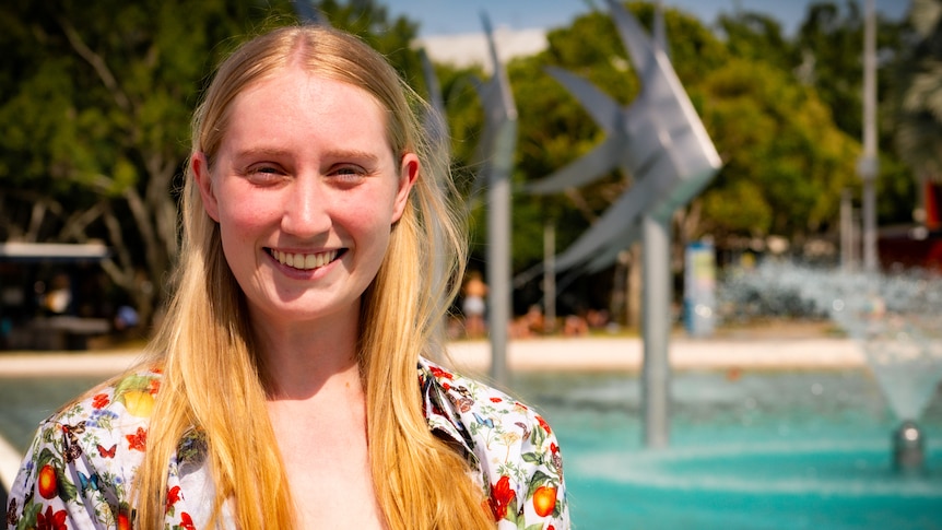 A young woman with long, straight, blonde hair stands in frnt of cairns lagoon