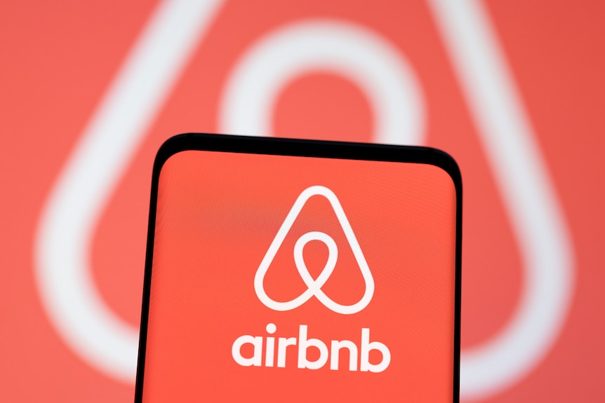 En la pantalla se muestra un teléfono inteligente con el logotipo de Airbnb delante del mismo logotipo.  