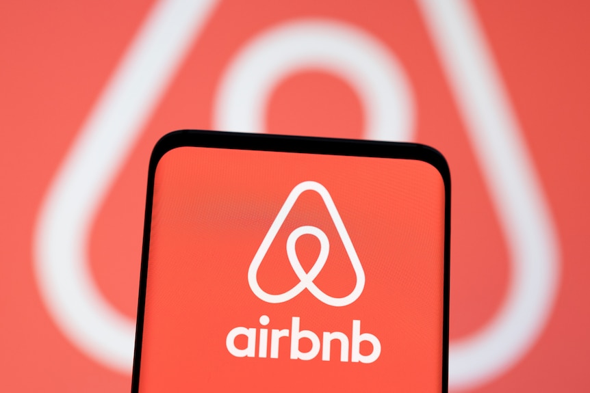 屏幕上显示在同一徽标前带有 Airbnb 徽标的智能手机。  