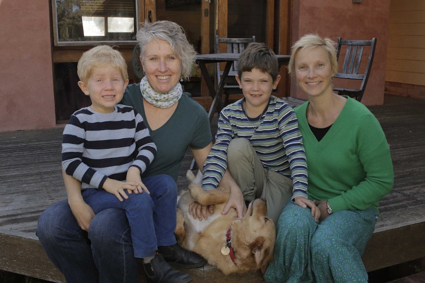 A family of four - two mothers and two sons - sit with a dog.