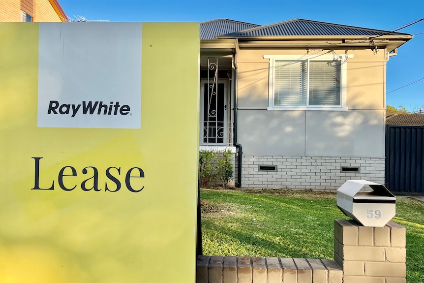 A yellow Ray White sign that says "lease" in front of a freestanding home.