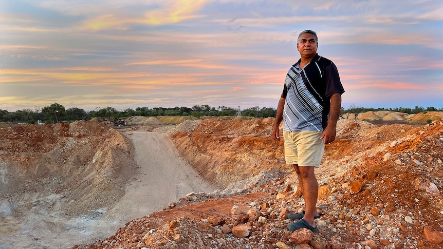 A First nations man standing in the outback smiling at the camera at sunset