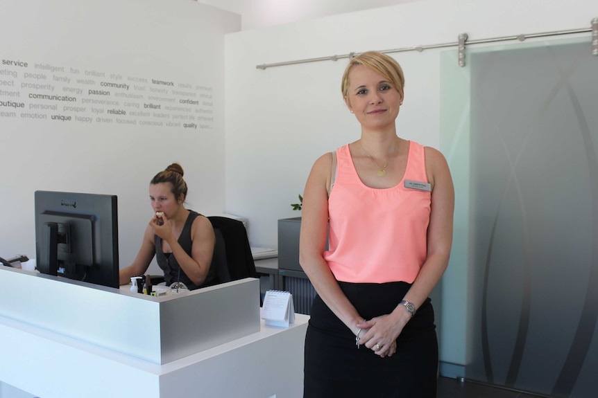 A woman stands in front of an office desk.