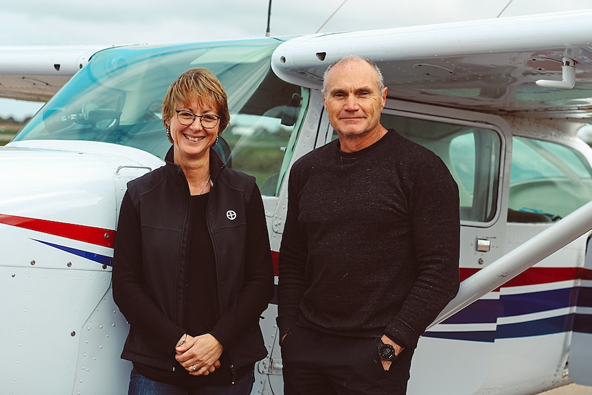 A man and woman smile in front of a light plane.