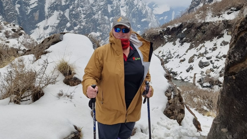 Woman with walking sticks and a yellow jacket on in mountains covered in snow.