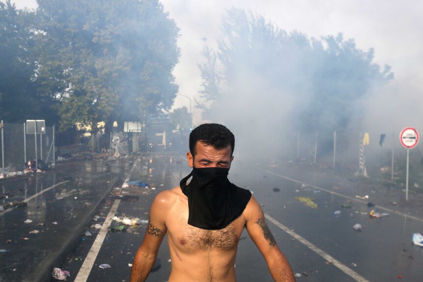 A migrant protests as Hungarian riot police fires tear gas