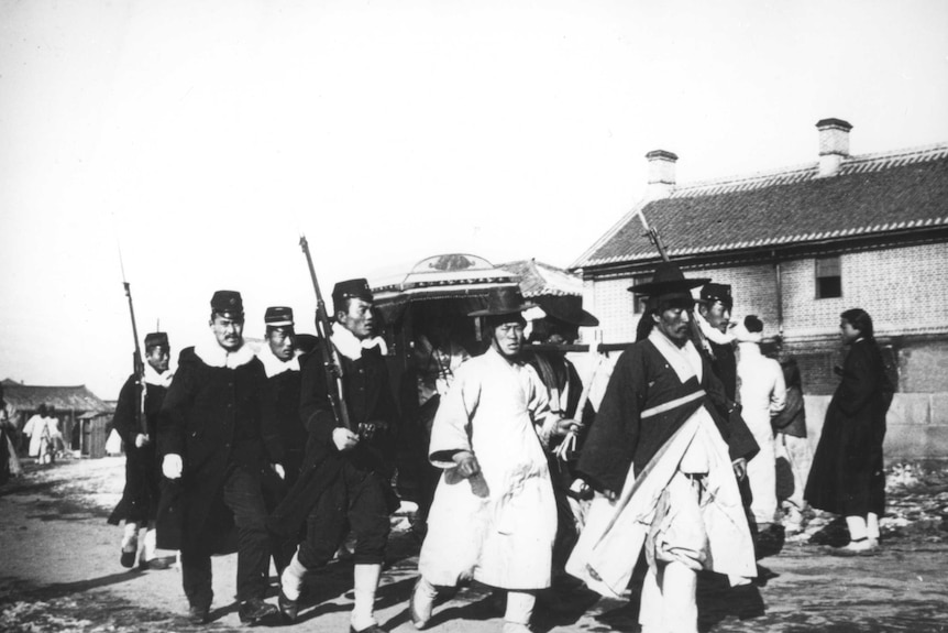 A group of Japanese officials in traditional dress walk on an unpaved road