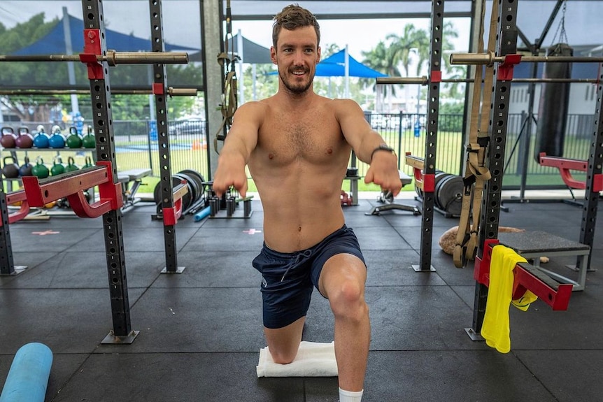 A shirtless man bending working out in a gym.