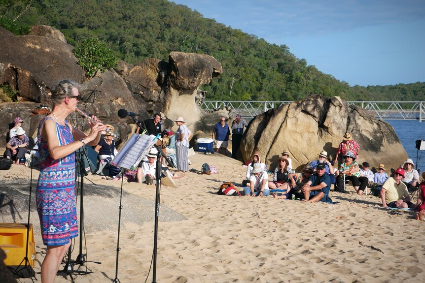 A woman plays the flute on a beach in front of a crowd of people