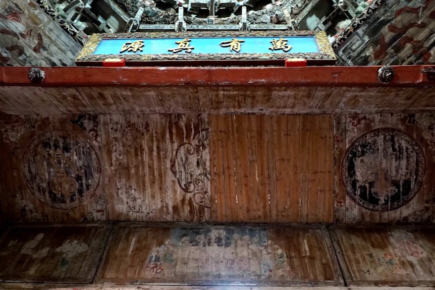Photo looks up at ceiling of structure with ornate decorations, four Chinese characters and a mural that has been sanded back