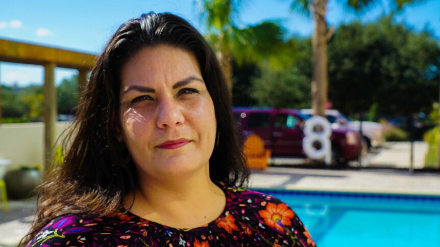 A tight headshot of a woman posing in front of a pool and palm trees.