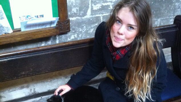 A young woman pats a cat sitting on a church pew.