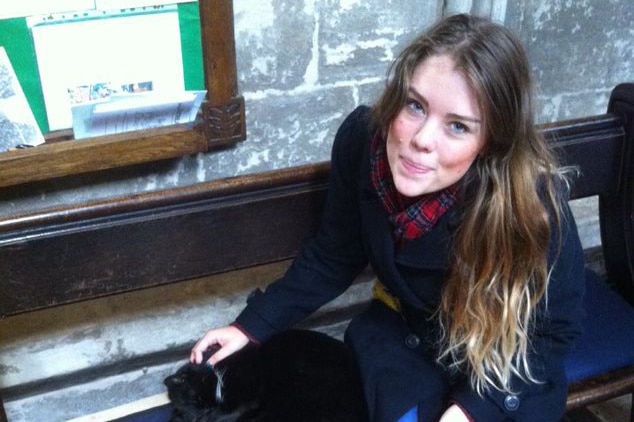 A young woman pats a cat sitting on a church pew.