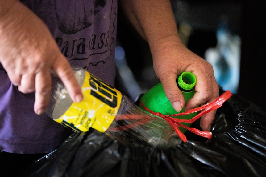 Hands sorting through a garbage bag full of empty bottles.