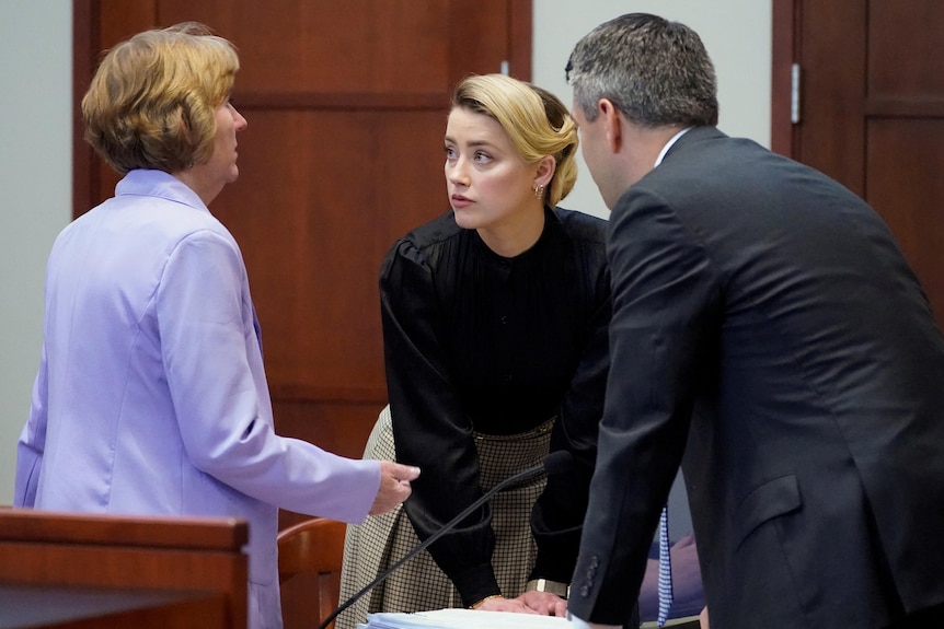 Amber Heard speaks with a man and a woman in a court room. 