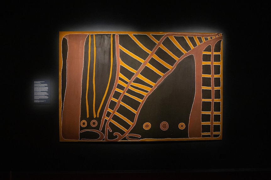 An Indigenous painting hangs in black room.