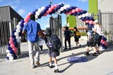 school kids in uniform walk through a gate lined with balloons with their parents