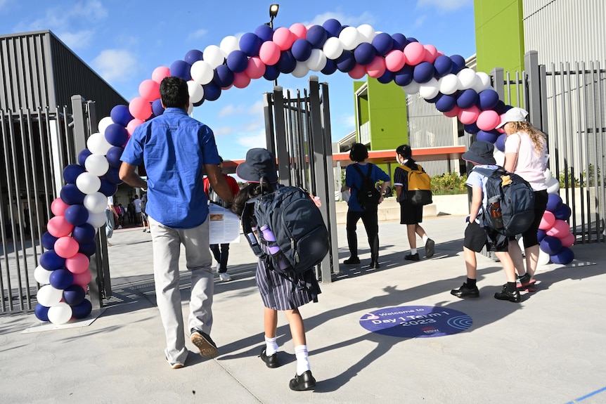 school kids in uniform walk through a gate lined with balloons with their parents