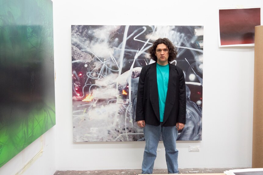 a man stands in front of an abstract painting