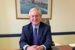 An image of Professor Ian Bennet sitting in a navy suit at a wooden table with a picture frame behind him