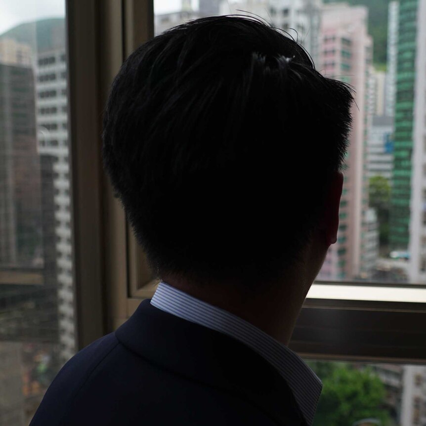 A man looks out a window at Hong Kong's skyline