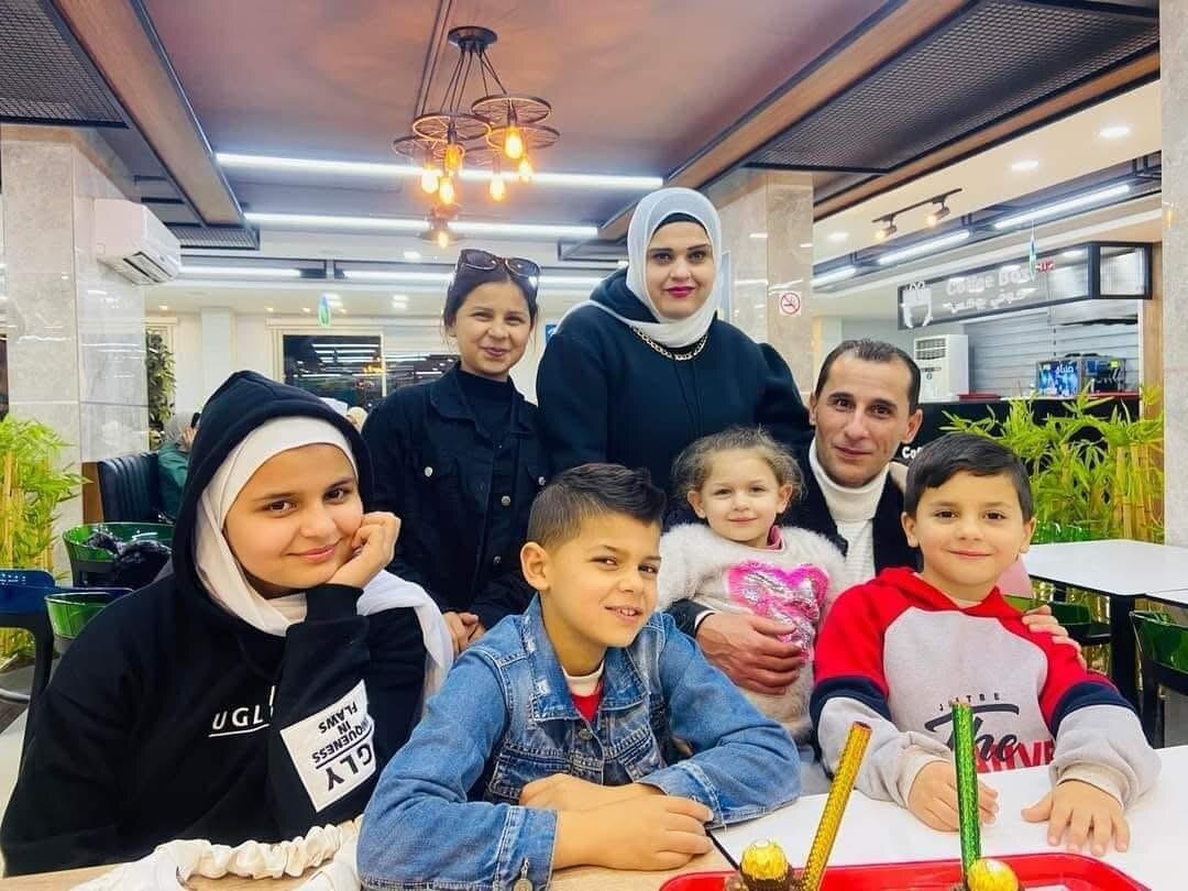 Tamim Muammar sits at a table with his five children and wife. They are smiling.