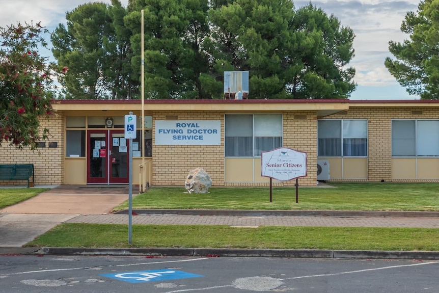 A light brown brick building on a cloudy day. Signs reading "Royal Flying Doctor Service" and "Senior Citizens" are out front