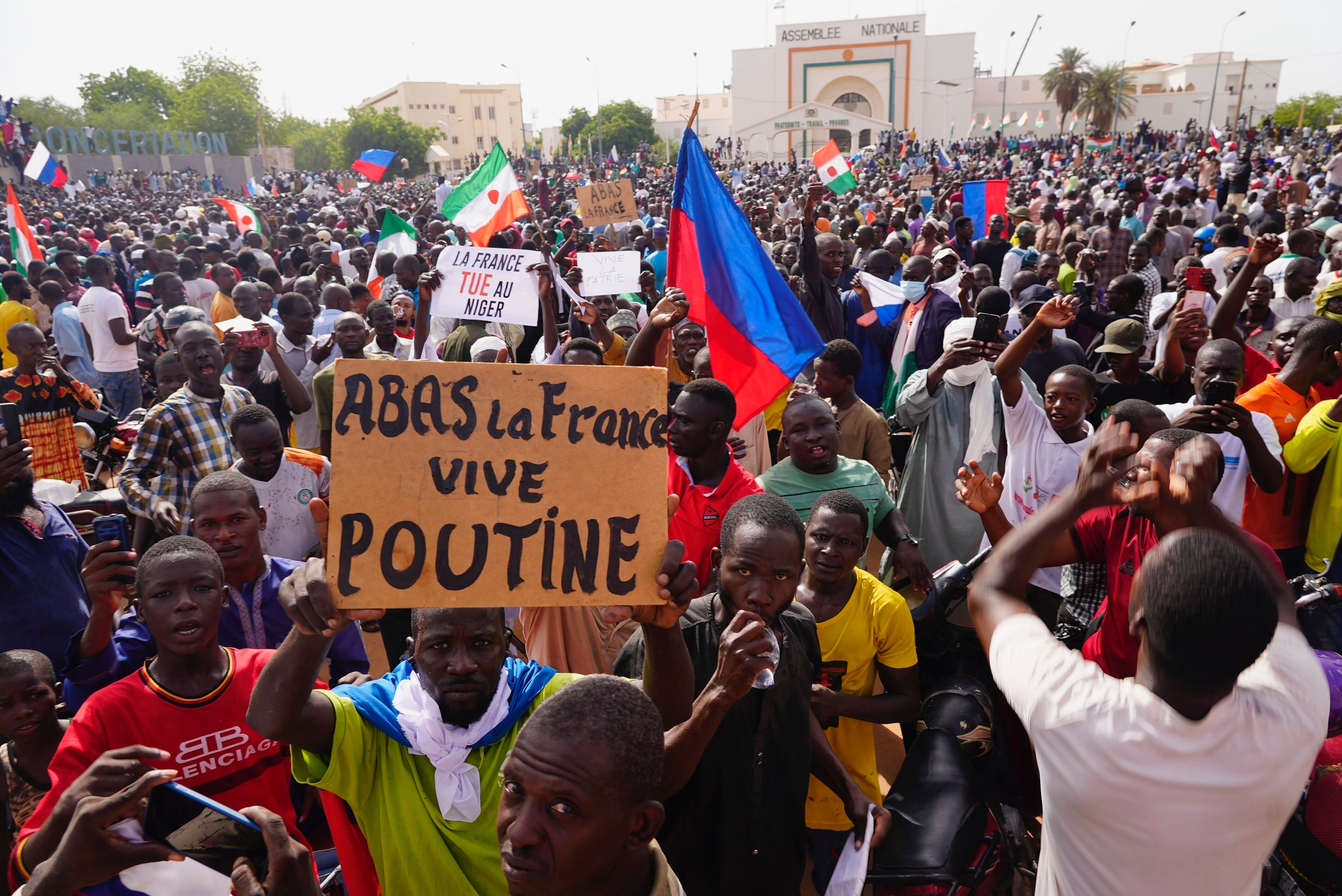 Among a crowd of protesters a man holds a sign that reads 'Down with France, long live Putin'