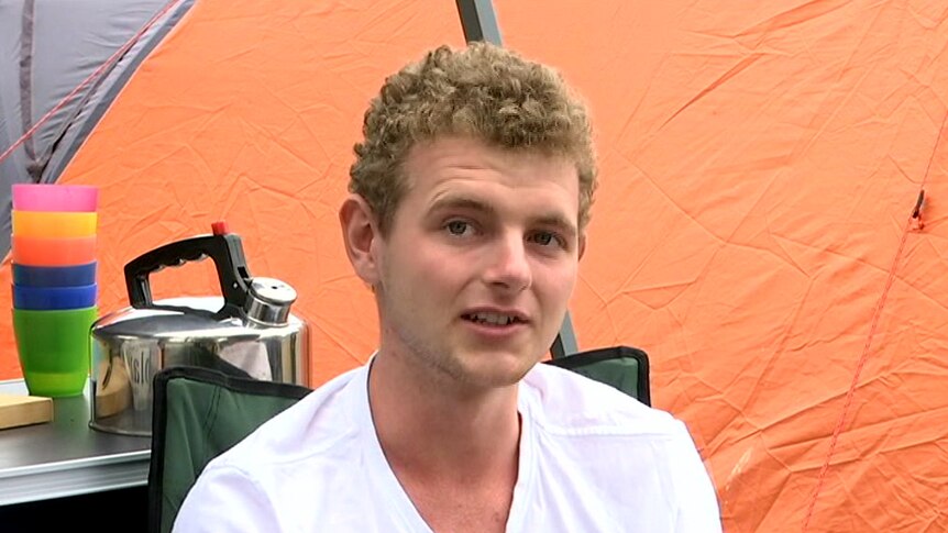 A young man sits in a camping chair at a caravan park.