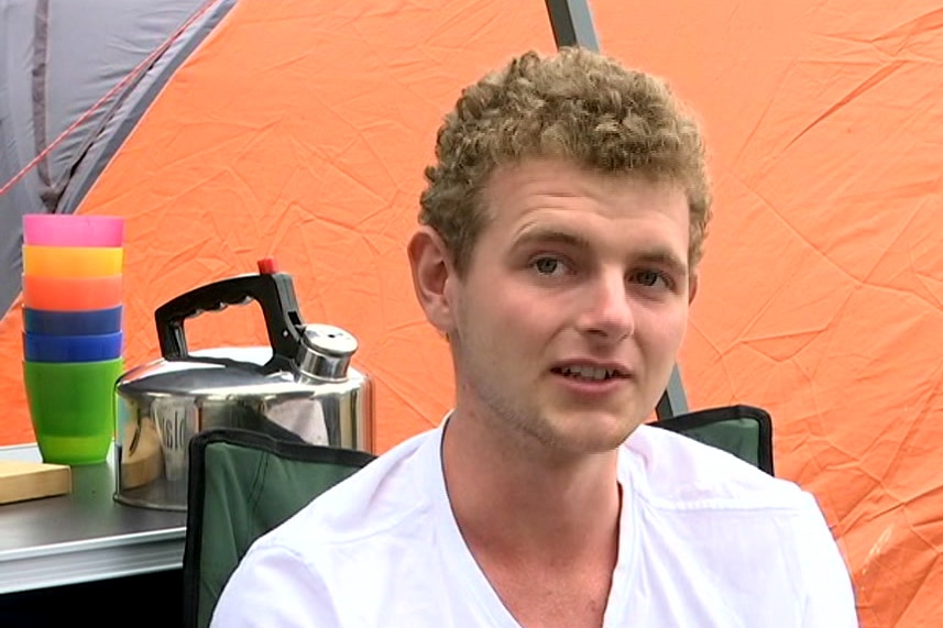 A young man sits in a camping chair at a caravan park.