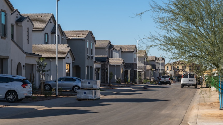 A street with lookalike houses lining one side and a dirt construction site on the other