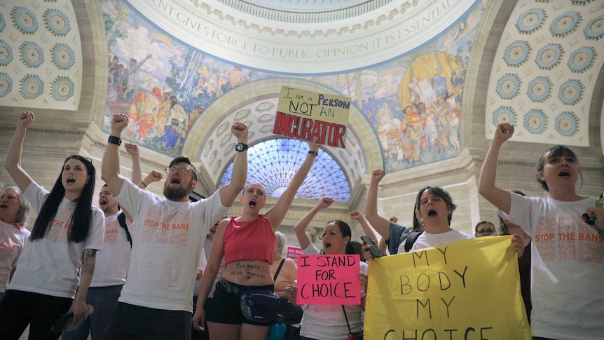 A group of protesters standing in a domed room holding signs reading "I am a person, not an incubator"