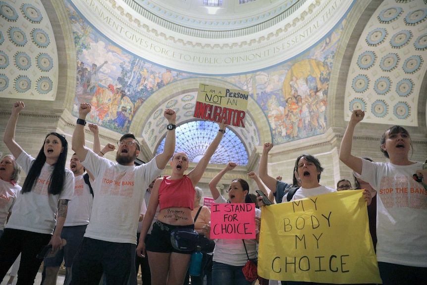 A group of protesters standing in a domed room holding signs reading "I am a person, not an incubator"