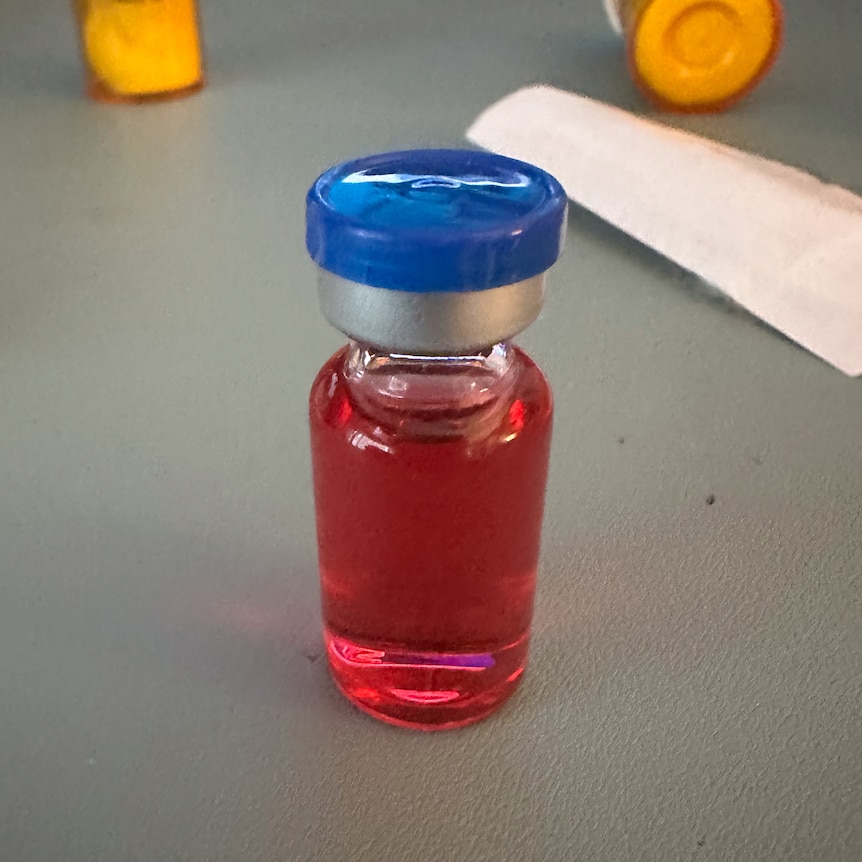 A small vial of red liquid sitting on a table.