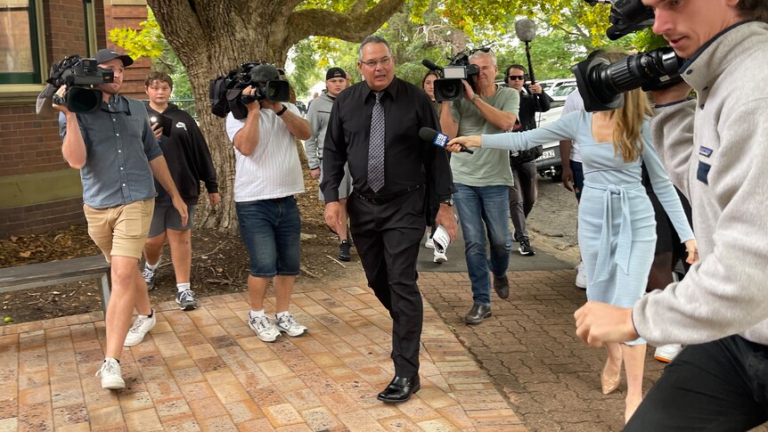 A man walking into a court surrounded by a media pack