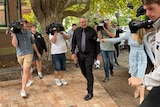 A man walking into a court surrounded by a media pack