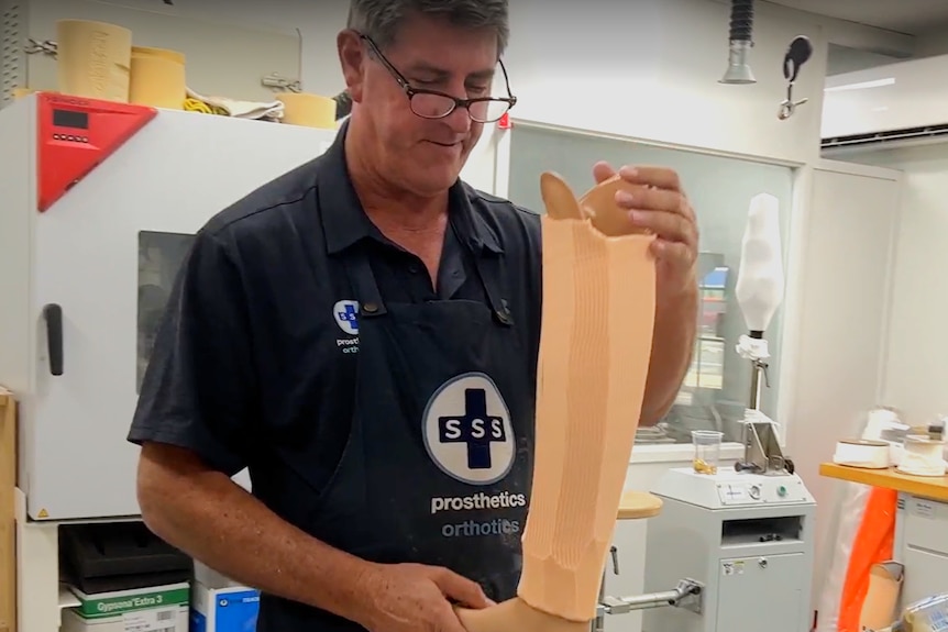 A man in a blue polo shirt handling a prosthetic leg mould on a workbench.