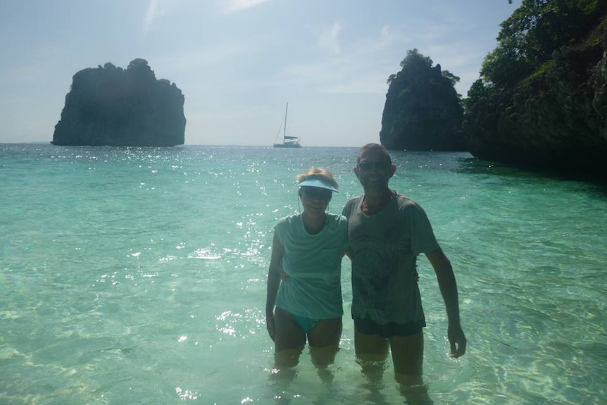 Del and Craig stand in clear blue water on tropical beach.