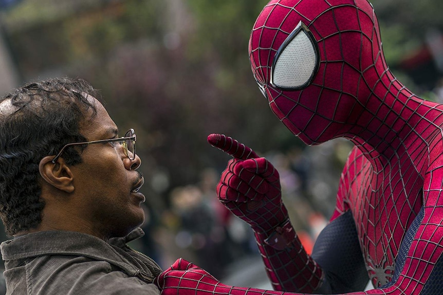 A man in a red and black Spider-Man suit points his finger at a man wearing glasses.