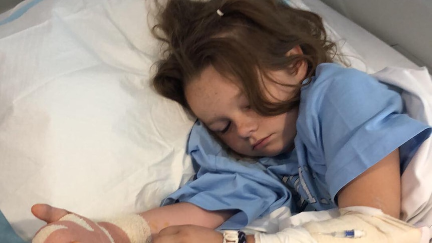 A young girl lies in a hospital bed.