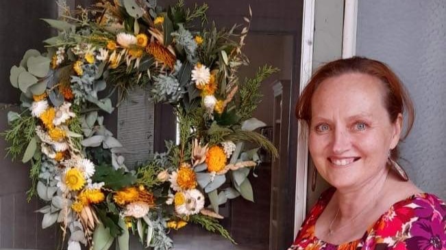 A lady standing next to a door that has a floral wreath hanging on it 