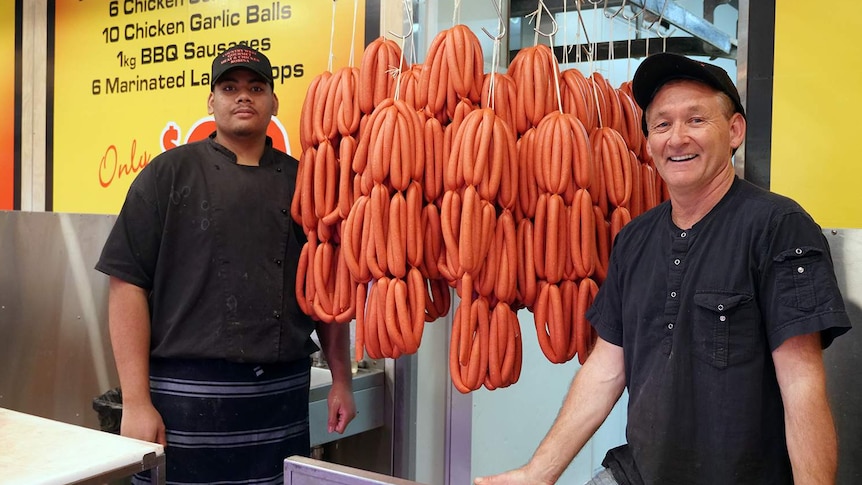 Two male butchers standing either side of racks of sausages