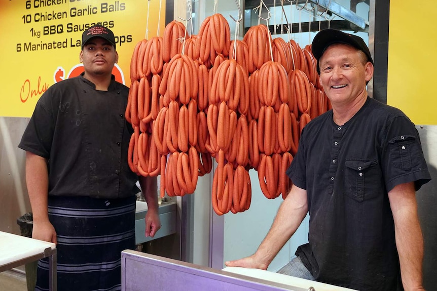 Two male butchers standing either side of racks of sausages
