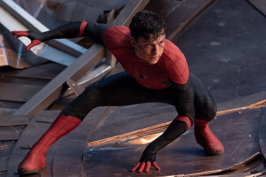 Un Spider-Man démasqué est accroupi dans une fente basse, une main sur le sol entre ses jambes et l'autre en l'air derrière lui.