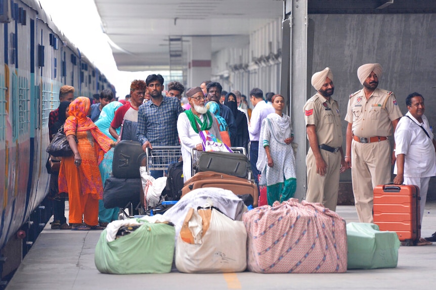 Looking at a train platform, you view a crowd of people with luggage alighting from a stopped train.